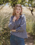 Woman wearing the Nesaea Top in black gingham with jeans standing in a field with tall grass and trees.
